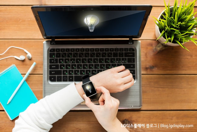 business, startup, idea, people and technology concept - close up of woman with smart watch and laptop computer on wooden table with light bulb on screens